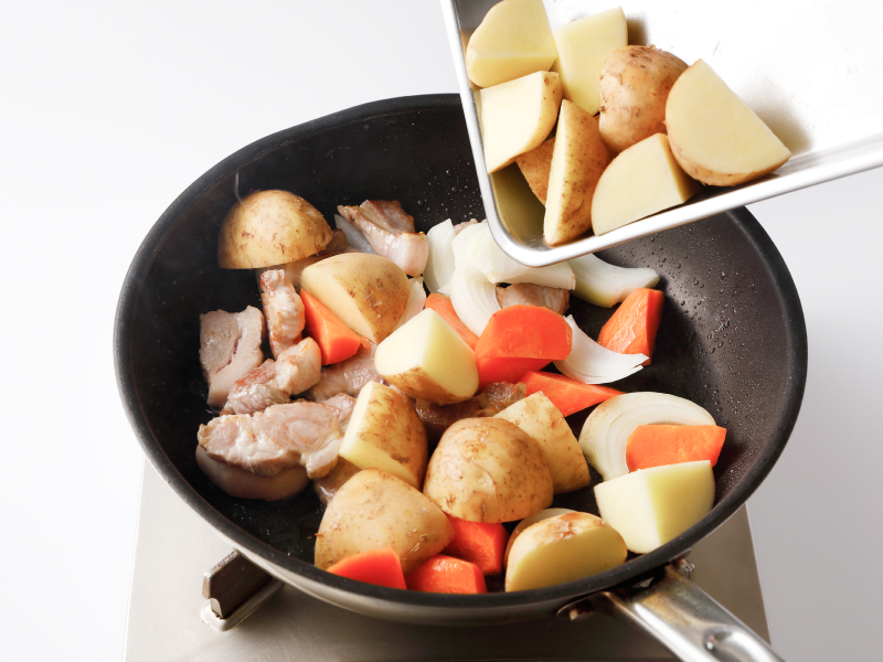 フライパンで豚肉、新じゃがいも、にんじん、玉ねぎを炒めている