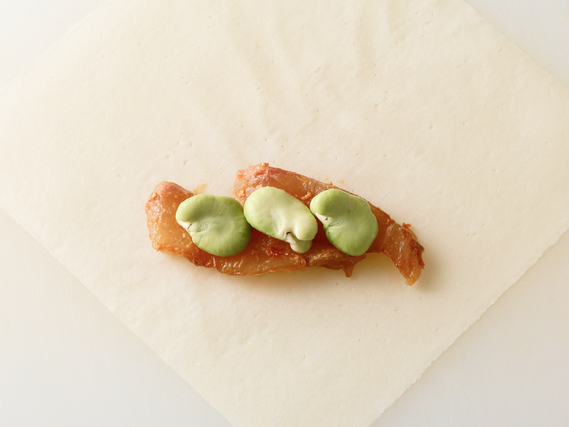 鯛の刺し身ふた切れととそら豆3粒を春巻きの皮に置き、包む
