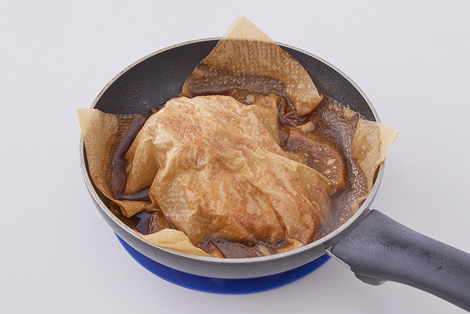 鶏胸肉をフライパンで調理している写真。ペーパータオルをかぶせ、煮汁をかけている