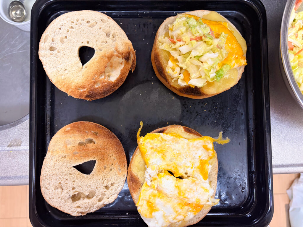 ラクレットチーズを乗せて焼いたベーグルに、卵焼きとコールスローを乗せている